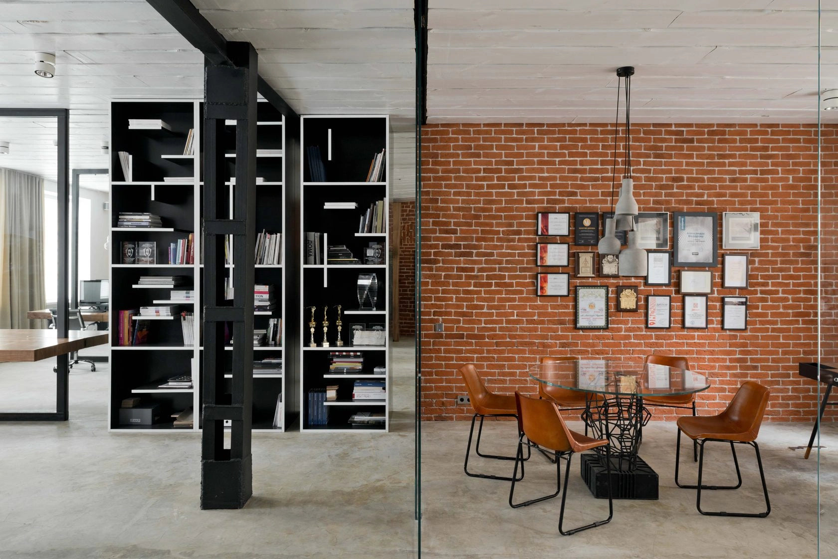 Modern office interior with bookshelves, a dining table, and framed pictures on a brick wall.